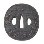 Séc. XVIII - Antiga e rara tsuba de formato ovalado em shakudo, liga de ouro e cobre, moldada e finamente cinzelada com motivos em relevo. Apresenta composições com ramos de diversas flores e frutas, sobre fundo texturizado e faixas horizontais representando pequenos degraus. Borda revestida por cinta de bronze fukurin. Período Edo. Início do séc. XVIII. Acompanha caixa em madeira. 7,3 x 7,0 x 0, 5 cm.