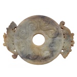 Belo e raro Disco Bi, artefato ritual chinês, em jade mesclado em tons claros cinzas e beges, de formato circular com centro vazado, ladeado e vazado por tigres. Apresenta decoração esculpida em alto relevo com dragões e estilizações. Possíveis infiltrações de outros minerais 14,0 x 10,0 x 1,0 cm.