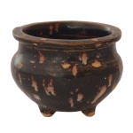 Raro incensório trípode em porcelana chinesa do tipo Jizhou de pasta clara, com coberta salpicada com manchas de cor bege sobre fundo preto, imitando plumagem de perdiz. Bojo globular com gargalo retraído, e borda revirada e saliente. Província de Jiangxi, sul da China. Dinastia Song (960-1279). Peça de coleção. 7,5 x 9, 5 cm.