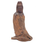 Estatueta chinesa esculpida em monobloco de madeira, com figura estilizada de Kwan Yin. Apresenta-se a deusa meio ajoelhada de lado, no chão, vestindo grande manto que lhe cobre o corpo inteiro. 22 x 13 x 8 cm.
