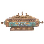 Incensório sino-tibetano para varetas de incenso, de formato retangular, em metal dourado com realces em esmaltes cloisonnés, usado em altares. Base chanfrada sustentando recipiente cilíndrico, ornado por arranjos florais e adornos estilizados. Extremidades arredondadas e realçadas por adornos simbólicos. Tampa construída com medalhões vazados, encimados por par de cabras centralizando ponteira. 14 x 33 x 7 cm.