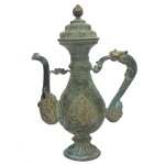 Jarra tibetana de formato balaústre, em bronze patinado com realces dourados, profusamente gravada e decorada com adornos florais e estilizações. Bojo no formato de gota, ornamentado em ambos os lados com figuras e animais em reservas. Bico recurvo e alça em S rematada com dragão. Apresenta gargalo em corneta, encimado por tampa cônica montada em degraus, e pega em ponteira. Base com anelado assentado sobre adorno esparramado. Marca estampada sob a base. 32 x 12 x 9 cm.