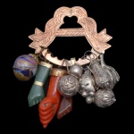 Penca de balagandã com fivela dourada encimada por folhagens. Apresenta e sustenta 8 amuletos, como frutas em metal repuxado e figas em pedra. 8 x 5 cm.