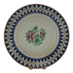 CHINA. DINASTIA QING (1644-1911). QUIANLONG (1736-1795) - Prato em porcelana chinesa da Companhia das Índias, ornamentado em esmaltes da Famille Rose com realces a ouro. Borda ornada por losangos floridos sobre fundo azul cobalto, centralizando buquê com peônias. 24 cm.