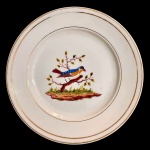 Prato em porcelana possivelmente francesa. Apresenta formato circular com frisos na borda e representação de pássaro ao centro. Decoração similar ao do Serviço Nast. 25 cm.