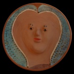 TOTA (Antônio Paschoal Regis  1923-2002) - Prato circular em barro / argila colhido na região onde o artista trabalhava. Estilo único, artesanal e artístico. O rosto possui feições suaves e lábios avermelhados. Os olhos são representados  por pequenos furos ou marcas escuras. A borda do prato apresenta um acabamento em tom de verde e azul com textura pontilhadas criando um contrastes com o terroso central, Ass. e datado 2000. Ceramista nascido em Tracunhaém, Pernambuco. Suas obras são caracterizada por um estilo expressionista com destaque para cabeças e figuras humanas marcantes.