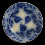 ENGLAND. Séc. XIX. Flow Blue - Prato em louça inglesa de formato circular. Apresenta decoração com elementos em tons de azul borrão. Centro com folhagens e borda com guirlandas.