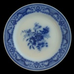 W. H. GRINDLEY  HARTINGTON. Circa 189 - Flow Blue - Prato raso em faiança inglesa decorado no padrão conhecido como azul borrão. Centro apresentando decoração com flores e folhagens. Marca da manufatura no verso. Livro, Flow .... pág. 190