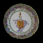 PEDRO ÁLVARES DE ABREU E SOUZA. Governador do Rio de Janeiro em 1775  Pires em porcelana chinesa da Companhia das Índias pertencente ao Ser viço do Governador do Rio de 1775, Pedro Álvares de Abreu e Souza. Apresenta centro com Brasão de Armas estilizado e bordas ondulada com padrão de arabescos, folhagens e flores predominando as cores, verde, rosa e vinho. Apresenta fio de cabelo presos por grampos. Séc. XVIII. 12 cm.