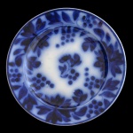 ENGLAND. Séc. XIX. Flow Blue - Prato em louça inglesa de formato circular. Apresenta decoração com elementos em tons de azul borrão. Centro com folhagens e borda com guirlandas. 21 cm.