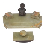 Tinteiro de mesa em ônix, de formato retangular. Figura central em bronze, compartimentos para tinta e caneta. Acompanha mata borrão Um dos compartimentos de tinta precisa de ajustes. Está solto. 16 x 40 x 20 cm (MT). 9 x 15 x 7 cm (mata borrão). 13 x 8 cm (escultura de bronze).