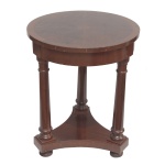 Mesa lateral ou mesa de apoio em madeira nobre com características que remetem ao estilo Império. Tampo de formato circular com superficie plana, sustentado por três colunas e que se conectam a uma base sólida  Séc. XX. 58 x 48 cm.