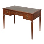 Mesa de escritório, estilo Louis XVI, em madeira nobre, ornada por frisos e almofadas caneladas. Tampo retangular, com quinas arredondadas, forrado em couro verde escuro. Caixa reta apresentando frente com gavetão ladeado por gavetas. Ilhargas e verso acompanhando o estilo. Pernas retilíneas no formato de colunas lisas, rematadas nas extremidades por adornos anelados. 76 x 110 x 60 cm. Este lote encontra-se na casa do comitente no Alto da Boa Vista, SP. A retirada deverá ser agendado previamente com o nosso escritório no telefone 11.5044.1228.
