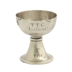 Taça em prata inglesa repuxada e cinzelada, com bojo liso semiesférico, gravado com os dizeres TTC Initium 1º 1918. Possivelmente prêmio de alguma competição. Haste em corneta com anelado, apoiada em base circular. Contrastes de Birmingham de 1911 e marca do prateiro Mappin & Webb. 5 x 5 cm. Peso 237 gramas.