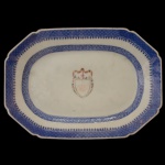 China. Séc. XVIII - Travessa retangular chanfrada em porcelana chinesa da Companhia das Índias, decorada em policromia de esmaltes. Borda ornada em azul cobalto com larga barra em treliças, filete em spearhead e friso geométrico. Apresenta ao centro brasão com monograma emoldurado e encimado por guirlandas floridas.