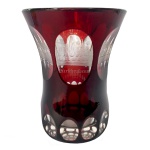 Copo em grosso cristal da Boêmia, de formato cônico com laterais levemente reviradas, revestido por overlay de cor grená intenso. Apresenta bojo lapidado com largos ovalados, alinhados e gravados com edificações religiosas e inscrições. Base retraída, circular e reta, ornada por janelas circulares 12 cm.