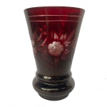 Copo em grosso cristal da Boêmia, de formato cônico reto, revestido por overlay de cor grená intenso. Apresenta composição floral à frente, gravada em tonalidades degradê. Base com anelado duplo e saliente, apoiada sobre fundo retraído. 13.8 cm.