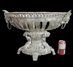 Europa final Séc. XIX. Excepcional centro de mesa de grandes dimensões e riquíssimo trabalho de cinzel. Apresenta-se sobre quatro pés ricamente trabalhados, duas figuras encostadas no fuste central à guisa de coluna que suportam a parte superior propriamente dita o nos mostra rico trabalho em vazados intercalados dando grande leveza ao conjunto de grandes dimensões. Em suas laterais à guisa de pega apresentam-se cabeças de leão estilizadas com suas argolas. Apresenta suporte interno para arranjo de flores ou outro uso que desejar. Medidas aprox. 40 cm de altura, 56 cm de comprimento e 35 cm de largura.