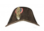 Chapéu Bicorne de feltro de castor marrom, conhecido pelo estilo en bataille, com as abas paralelas aos ombros. Usado durante a era napoleônica o estilo permitia fácil reconhecimento no campo de batalha. Apresenta ainda escarapela com medalha. Medidas aprox. 23 cm de altura, 40 cm de largura e 18 cm de profundidade.