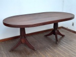 MOBILIÁRIO - IMPONENTE MESA DE JANTAR OVAL ANTIGA COM DUAS BASES PEDESTAL - Magnífica mesa de jantar de época, confeccionada em madeira maciça de tonalidade escura, que se destaca pela sua imponência e design clássico. Com um tampo oval de generosas dimensões de 190 cm de comprimento por 108 cm de largura, esta peça é ideal para acomodar confortavelmente a família e convidados. A mesa é sustentada por duas robustas bases centrais tipo pedestal, ricamente torneadas e com pés elegantemente curvados, que não só garantem grande estabilidade como também conferem um visual sofisticado e atemporal. Com 73 cm de altura, esta peça é perfeita para ser o ponto focal de uma sala de jantar clássica ou contemporânea. A pátina natural da madeira atesta sua autenticidade e história, tornando-a um item de valor e beleza duradoura. Med.73x190x108 cm. Marcas do tempo.