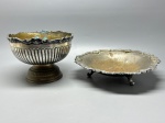 METAL - Par de fruteiras/centros de mesa em metal espessurado a prata  estilo clássico europeu. Conjunto decorativo formado por dois centros de mesa em metal espessurado a prata, ambos com desenhos de bordas repuxadas e decoração em relevo. Um dos centros possui base elevada com frisos verticais em caneluras e borda rococó ricamente detalhada. O outro repousa sobre três pés curvos e apresenta borda recortada com elementos florais. Ambos com sinais de oxidação e pátina do tempo, que atestam a antiguidade das peças. Med. 15x21 cm e 7x28 cm. Desgastes.