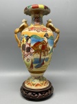 PORCELANA ORIENTAL - Belíssima e antiga ânfora de porcelana japonesa Satsuma, adornada com rica e delicada pintura policromada, contendo douração, representando cena tradicional. Acompanha peanha em madeira. Med 24x15 cm.
