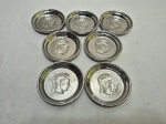 Jogo de 7 descansos de copo em porcelana porcelana com baixo relevo de cabeça romana e pintada de prata. Medindo 10cm de diâmetro.