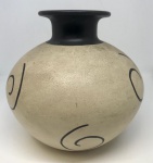 Charmoso vaso artesanal em cerâmica, com um design único e contemporâneo. A peça apresenta um corpo arredondado em tom creme ou bege claro, contrastando elegantemente com o bocal e a base em preto fosco. A superfície do vaso é adornada com padrões abstratos e orgânicos em preto, que adicionam um toque artístico e moderno. Mede: 17x17.