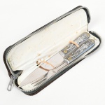 CUTELARIA, conjunto trinchante para carne com dois (2) itens: 1 faca e 1 garfo, lâmina em aço inox, cabo em metal prateado, detalhes em dourado, ornamentação figurativa e vegetalista em relevo, Indústria Argentina, acondicionadas em capa de couro ou símile com fechamento por zíper, medindo a maior peça 12 cm comprimento, sinais de uso, vide foto.