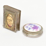 COLECIONISMO, duas (2) caixas miniaturas distintas confeccionadas em folha de flandres: 1 porta terço com lito do Velho Guerreiro (Chacrinha), medindo 5 x 4 x 1,2 cm; 1 porta comprimidos com lito floral policromada na tampa, possui divisória interna, medindo 4,5 cm diâmetro, ambas com sinais de uso e oxidação, vide foto.