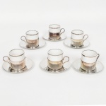 PORCELANA E METAL PRATEADO, seis (6) xícaras para café, cilíndricas, tonalidade branca, arremates com frisos prateados, duas manufaturas distintas POZZANI e RENNER, monture e pires vazado, sinais de uso, vide foto.