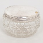 CRISTAL E METAL PRATEADO, um (1) antigo potiche com tampa, incolor e translúcido, lapidação geometrizada, fundo estrelado, possivelmente CRISTALERIE BACCARAT (fundada em 1765 pelo Bispo de Metz na região de Baccarat como Verrerie de Saint Anne; em 1815 foi vendida, junto com outras Verreries da região, para Gabriel D'Artigues e virou Voneche-Baccarat, passando a fabricar cristal de alta qualidade; em 1822 foi vendida e virou Compagnie des Cristalleries de Baccarat, mantendo o nome Voneche até 1843, atualmente é a Cristallerie mais importante da França), tampa com borda canelada na horizontal, medindo 10 cm diâmetro e 6,5 cm altura, sinais de uso, vide foto.