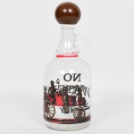 VIDRO, uma (1) garrafa, incolor e translúcida, ornamentação esmaltada representando charrete, tampa rosqueável com acabamento em madeira torneada, legenda: No Water Whisky Only, medindo 27 cm altura, ideal para adornar bar, sinais de uso, vide foto.