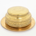 METAL DOURADO, um (1) potiche com tampa e presentoir, ornamentação relevada em perolados e elementos vegetalistas, tampa com silhueta representando cupido, sem marca de manufatura aparente, medindo 12,5 cm diâmetro e 7 cm altura, presentoir 16,5 cm diâmetro e com pequeno furo na borda, sinais de uso, vide foto.