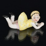 ESCULTURA, uma (1) antiga representando menina deitada, confeccionada em biscuit, policromada, medindo 8 cm comprimento, ideal para coleção de bibelôs, vide foto.