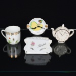 PORCELANA, quatro (4) itens diversos: 1 polvilhador no formato de bule com relógio, medindo 9 cm altura; 1 placa com a legenda FELICIDADE, marca DISMOPE, medindo 11,5 x 7 cm; 1 xícara sem o pires, lembrança de Valença, ornamentação floral policromada; 1 cinzeiro ornado em policromia com dançarina do Can  Can, policromado, arremates a ouro, marca EMANO (Janowitzer, Rio de Janeiro, RJ, 1931 a 1977, revendedor e decorador de porcelana de outras fábricas), medindo 8,5 cm diâmetro, vide foto.