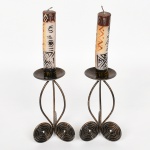 DIVERSOS, par (2) castiçais confeccionados em aramado vergado e chapa, patina na tonalidade bronze, medindo 14 cm altura, mais as velas com decoração tribalista, uma delas se encontra quebrada, vide foto.