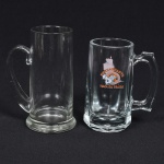 VIDRO, duas (2) canecas distintas, incolores e translúcidas, para chopp ou cerveja, uma delas com propaganda do Restaurante Toca da Traíra, medindo a maior 17 cm altura, sinais de uso, vide foto.