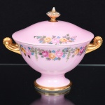 PORCELANA, uma (1) pequena terrina de pé baixo com tampa, ornamentação floral policromada sobre fundo na tonalidade rosa, pega da tampa na forma de pinha, generosos arremates a ouro com falhas, sem marca de manufatura aparente, medindo 16 cm altura, vide foto.