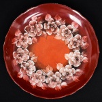 PORCELANA, um (1) prato decorativo com ornamentação floral policromada sobre fundo dito sangue de boi, pintado a mão pelo atelier ZAIRA, manufatura SCHMIDT (Pomerode, SC; Mauá, SP; Campo Largo, PR, fundada em 1945, ainda em atividade, maior fábrica de porcelana da América Latina), medindo 26,5 cm diâmetro, vide foto.