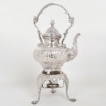 METAL PRATEADO, um (1) samovar com ornamentação relevada, cinzelada e burilada em volutas e elementos vegetalistas, base com pés terminando em garras, pega da tampa na forma de pinha, falta o queimador, medindo 45 cm altura, sem marca de manufatura aparente, sinais de uso, vide foto.