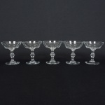 CRISTAL, cinco (5) taças de pé alto para champanhe, incolores e translúcidas, bojo com lapidação dita dedão,fuste com colunetas sobrepostas, base em bolacha, duas delas com bicados na borda, medindo 11 cm altura e 10 cmdiâmetro, sinais de uso, vide foto.