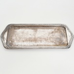 AÇO INOX, uma (1) travessa quase retangular, fundo liso, borda relevada em corda, conchas e elementos vegetalistas, sem marca de manufatura aparente, medindo 33 x 14 cm sinais de uso, vide foto.