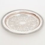 AÇO INOX, uma (1) travessa oval de borda alta, fundo em baixo relevo representando pérgulas, volutas e elementos vegetalistas, borda relevada em corda, sem marca de manufatura aparente, medindo 29 x 22 cm sinais de uso, vide foto.