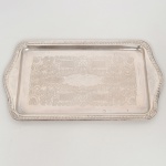 AÇO INOX, uma (1) travessa quase retangular, fundo em baixo relevo representando pérgulas, volutas e elementos vegetalistas, borda relevada em corda, conchas e elementos vegetalistas, sem marca de manufatura aparente, medindo 36 x 20 cm sinais de uso, vide foto.