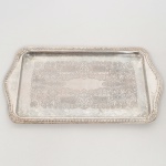 AÇO INOX, uma (1) travessa quase retangular, fundo em baixo relevo representando pérgulas, volutas e elementos vegetalistas, borda relevada em corda, conchas e elementos vegetalistas, sem marca de manufatura aparente, medindo 36 x 20 cm sinais de uso, vide foto.