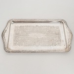 AÇO INOX, uma (1) travessa quase retangular, fundo em baixo relevo representando pérgulas, volutas e elementos vegetalistas, borda relevada em corda, conchas e elementos vegetalistas, sem marca de manufatura aparente, medindo 36 x 20 cm sinais de uso, vide foto.