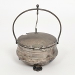 METAL PRATEADO, um (1) porta queijo ralado, tampa articulada com abertura basculante, detalhes relevados em conchas, interior com recipiente em polímero na tonalidade branca, manufatura EBERKOC, medindo 10 cm diâmetro e 14,5 cm altura, sinais de uso, vide foto.