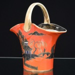 PORCELANA JAPONESA, um (1) vaso modelado no formato de cesta, ornamentação pintada a mão com paisagem lacustre policromada sobre fundo na tonalidade coral, representando pagodes, montanhas, salgueiros, ponte, figura, barco, etc., generosos arremates a ouro já com sinais de desgaste, marca da manufatura NORITAKE (1858 - Japão assinou o Tratado de Amizade e Comércio com os EUA, Holanda, Rússia, Reino Unido e França; 1867 fim do Shogunato e início da era Meiji; 1876 - Morimura-Kumi formada em Tóquio para exportação Os Morimuras & The Okuras unidos, a Companhia Hinode se estabelece na cidade de Nova York para o varejo; 1879 - A Companhia Hinode fecha. Morimura Bros & Co., se estabelece em Nova York; 1880 - Hiroses juntou-se a Morimura-Kumi em Tóquio; 1882 - Morimura Bros & Co., decidiu ser o atacadista; 1884 Morimura-Kumi subcontrata atelieres de decoração em porcelana nas cidades de Tokyo, Nagoya e Kyoto; 1918 - Morimura-Kumi é reorganizada como Morimura Bros, Inc.; 1921 - Morimura Bros de New York é incorporada a Morimura Bros, Inc. De Tokyo; 1947 - Noritake Co., Inc. com sede em Nova York; 1981 - Nome japonês da Companhia alterado para Noritake Co. Limited), além de selo de consumo do Brasil parcialmente legível, medindo 18 cm altura até a alça, sinais de uso, vide foto.