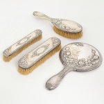METAL PRATEADO, parte de antigo conjunto para toucador com cinco (5) itens: 1 moldura para espelho de mão (sem o espelho); 3 escovas distintas; 1 pente (alguns dentes quebrados), ornamentação relevada no padrão Império Napoleônico com frisos intercalados por X, rosas e outros adereços, puncionada ALPACCA, medindo a maior peça 25 cm comprimento, sinais de uso, vide foto.